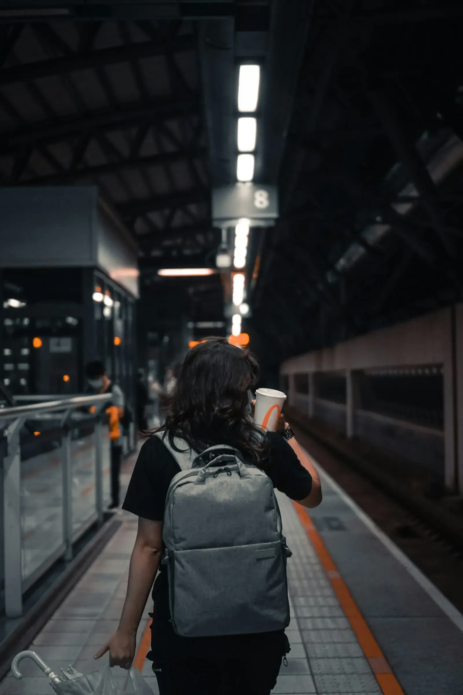 Woman with a backpack and coffee waiting on a train platform