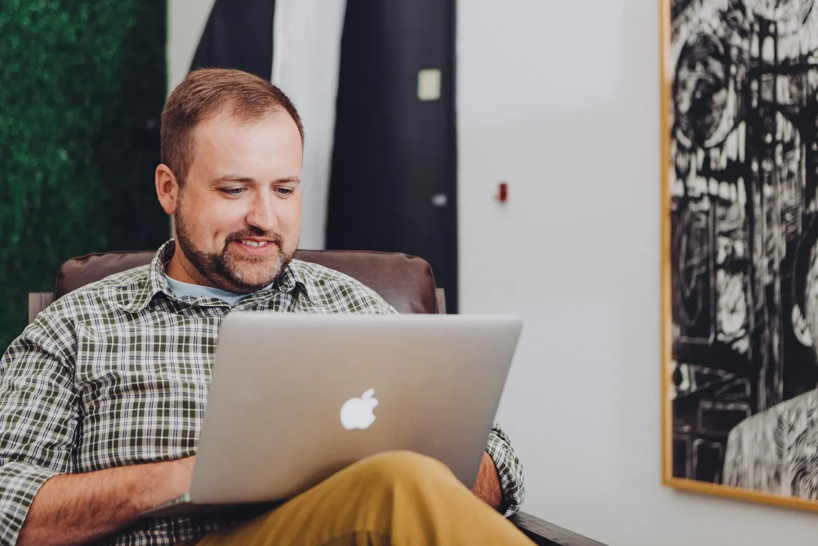 Smiling man working on a laptop in an armchair