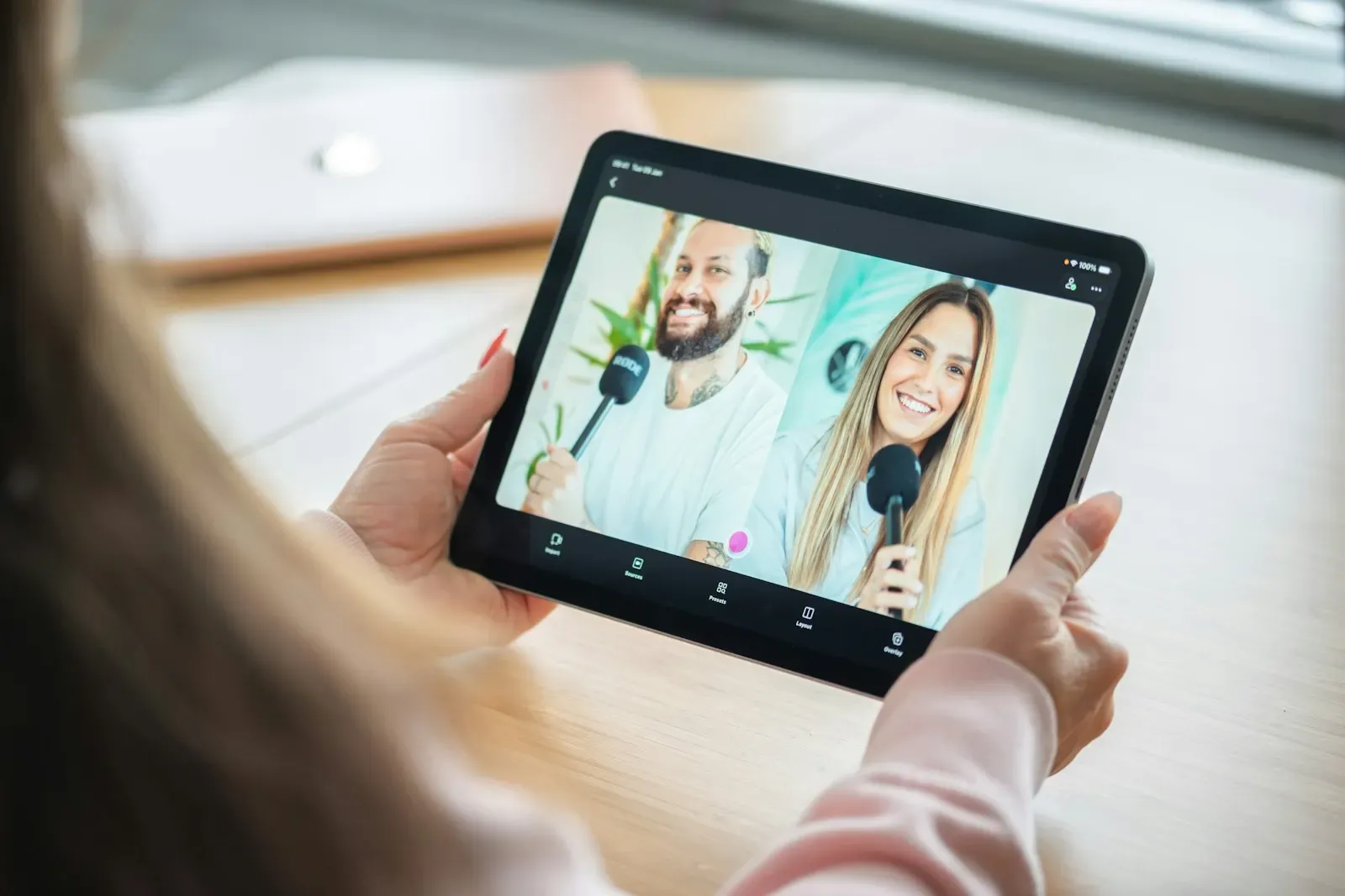 Hands holding a tablet showing a video call with two smiling people
