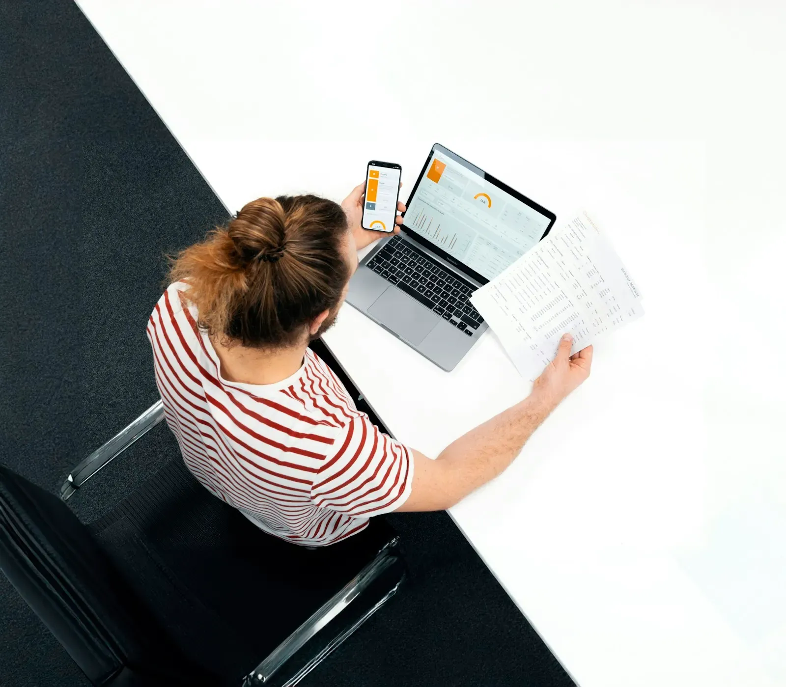 Person at a desk reviewing papers next to a laptop and phone