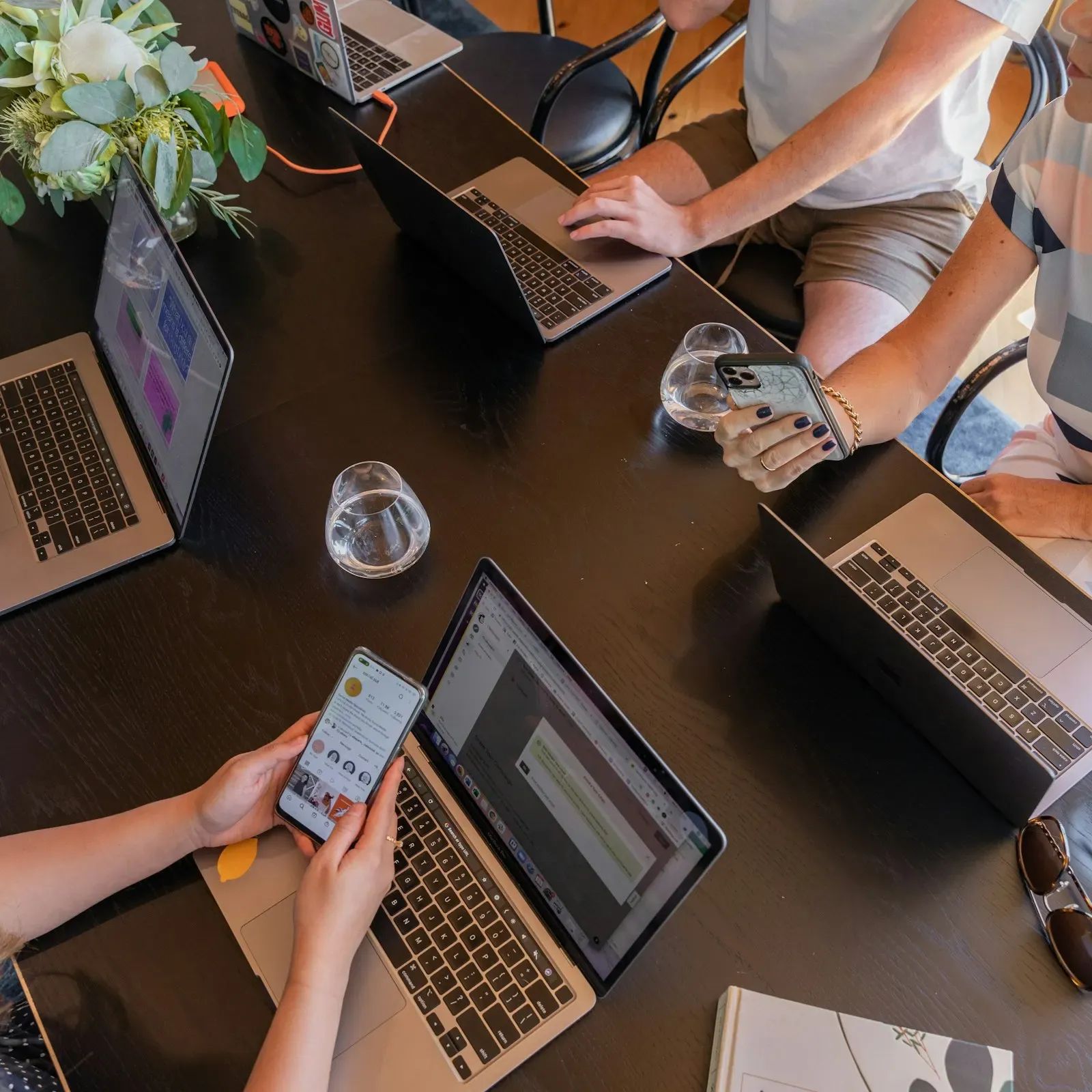 Sales team working on laptops and phones around a dark table