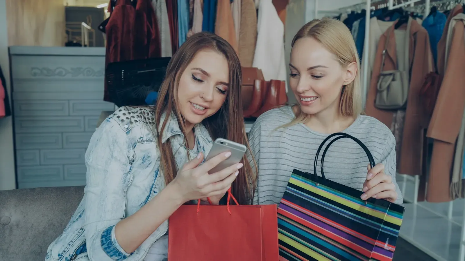 Two friends with shopping bags looking at a phone together