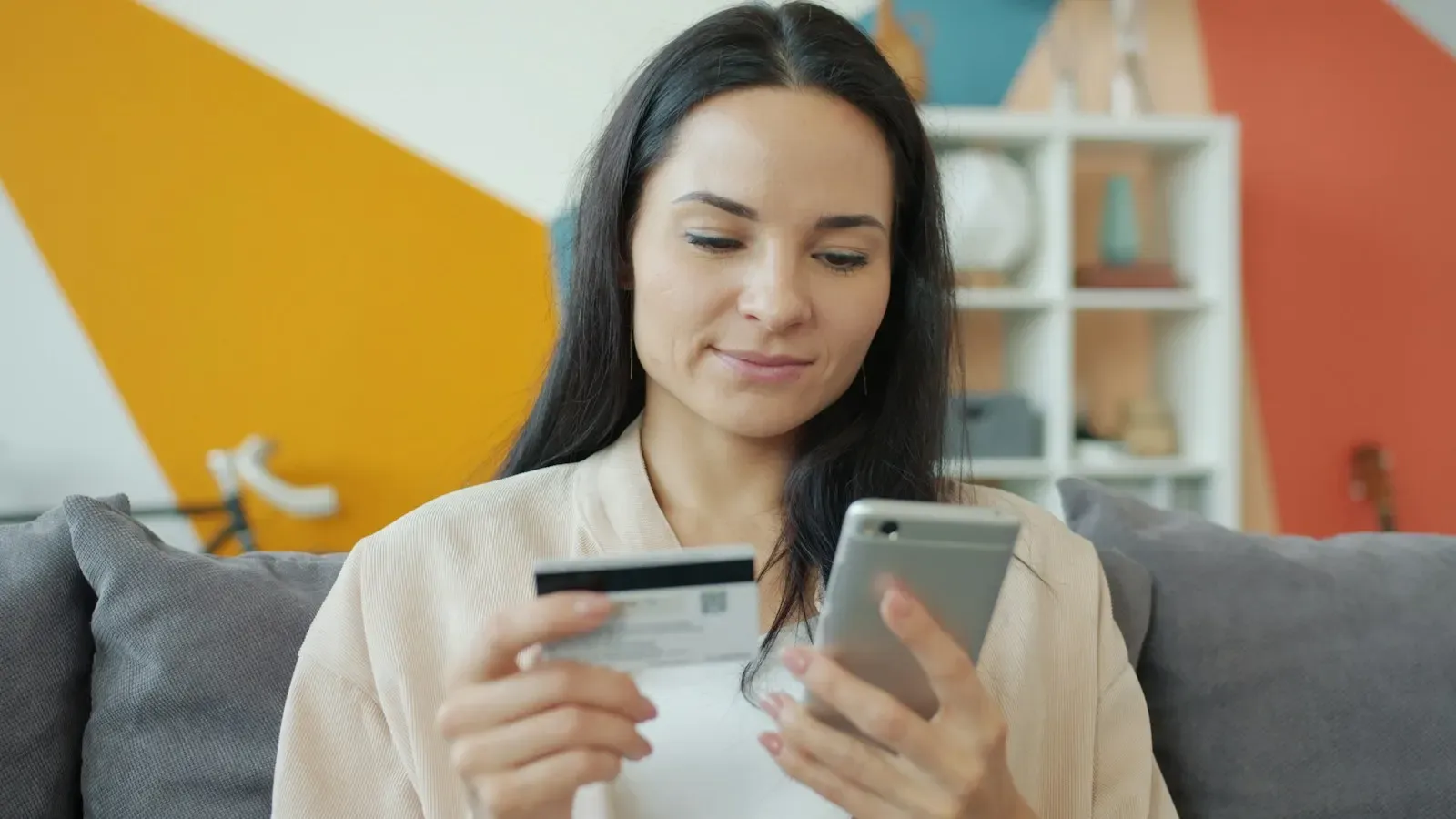 Woman on a sofa shopping online with her phone and a bank card