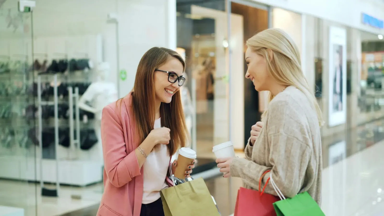 Two women with coffee cups talking in a shopping center