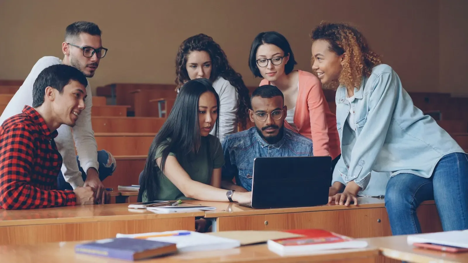Students gathered around a laptop in a lecture hall