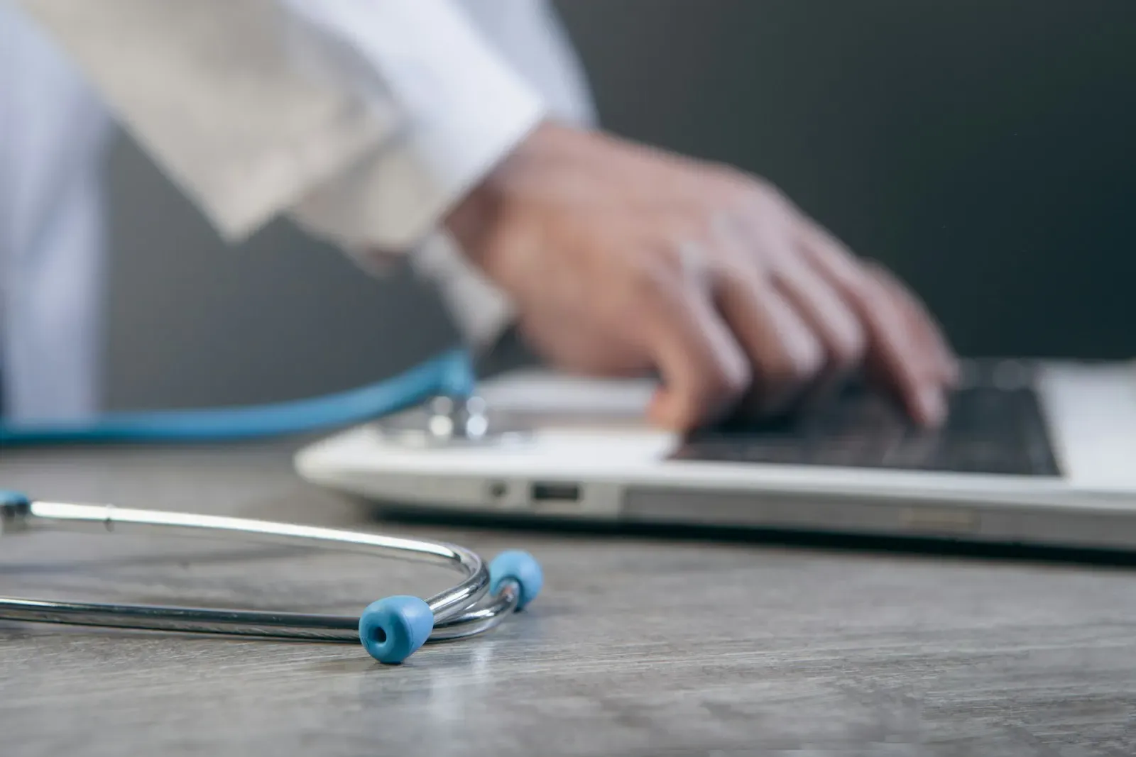 Clinician typing on a laptop with a stethoscope on the desk