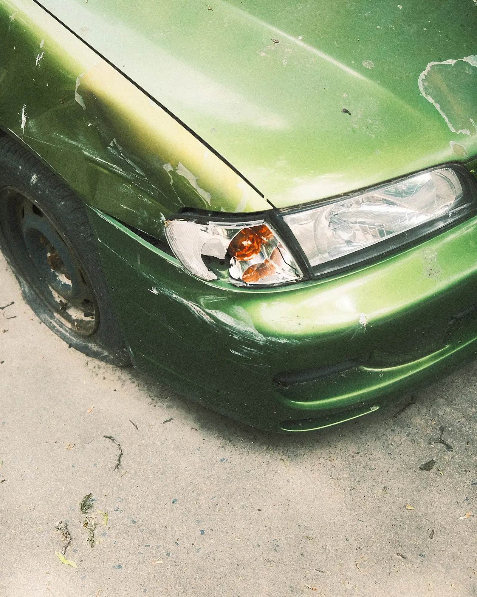 Green car with a dented front bumper