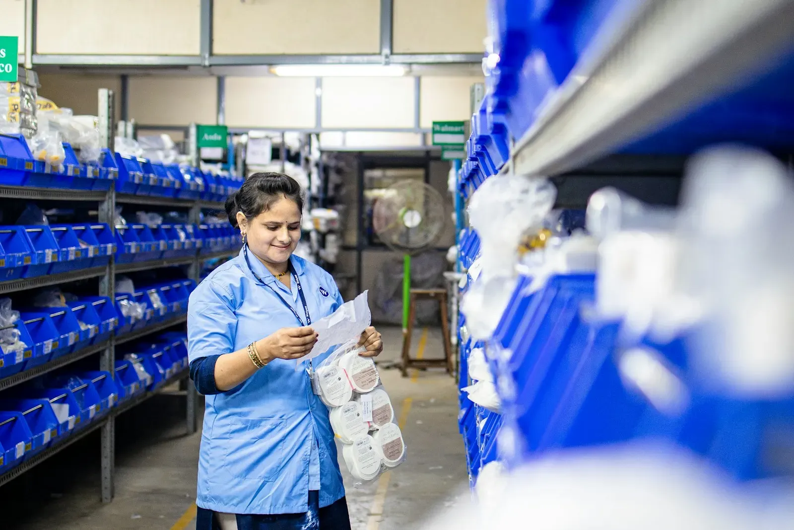 Warehouse worker checking parts against a list beside blue storage bins