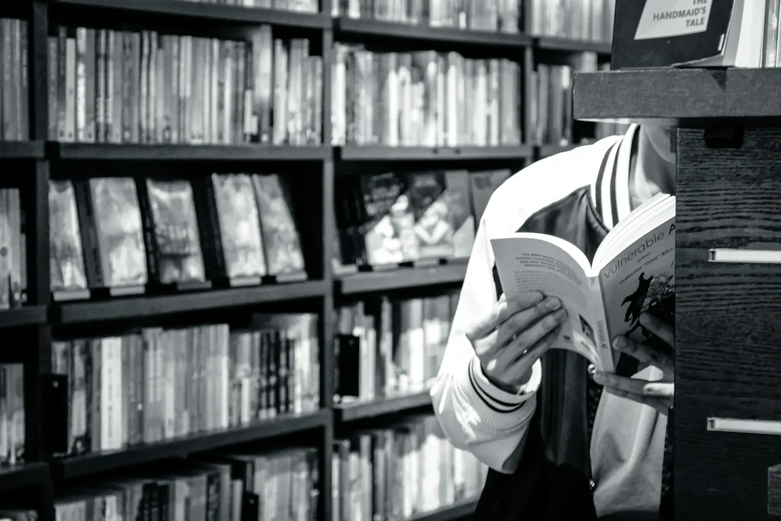 Person reading a reference book between library shelves