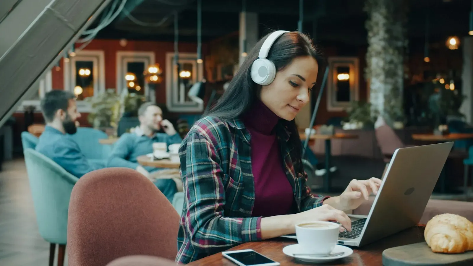 Writer with headphones drafting on a laptop in a cafe