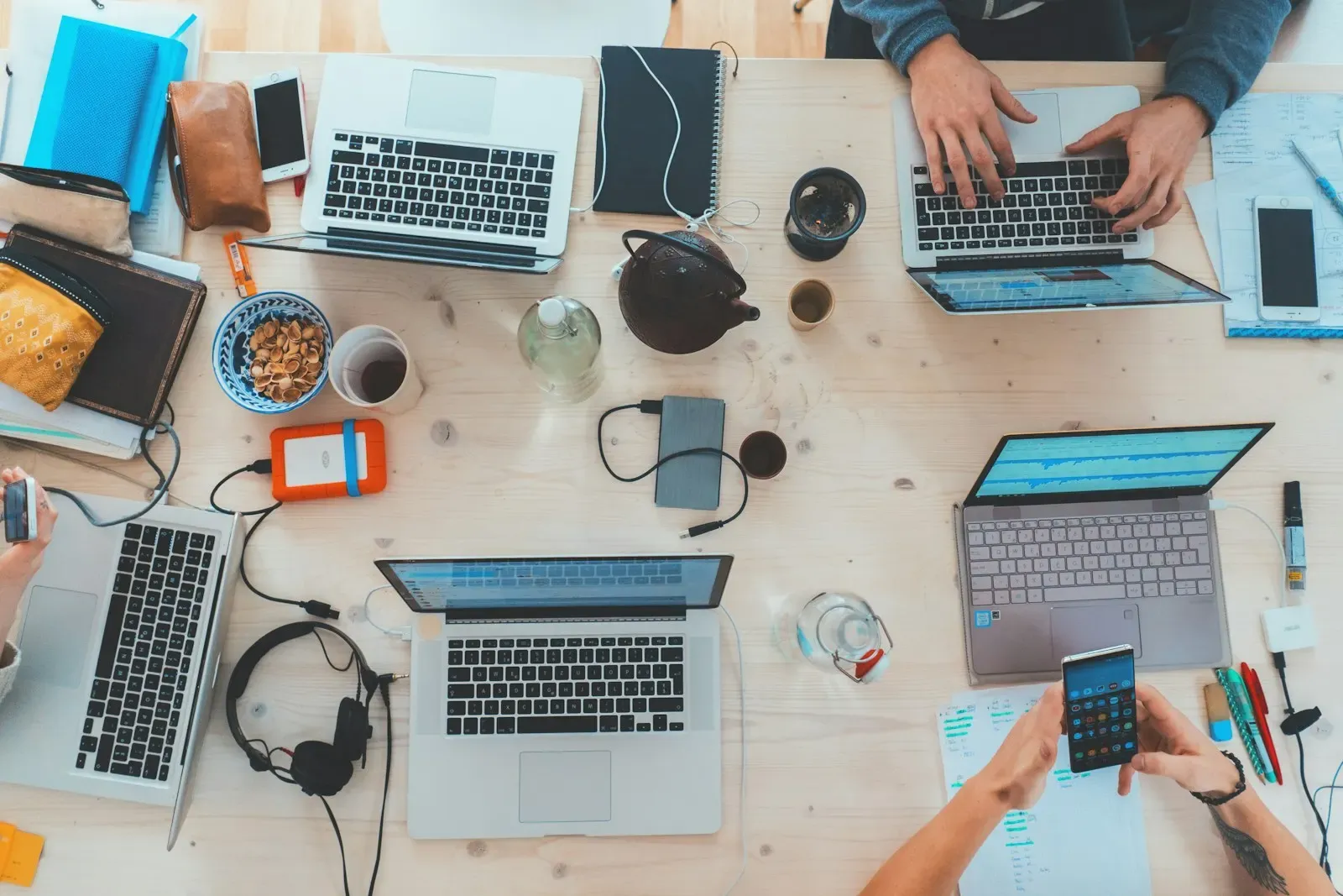 Laptops, phones and notebooks on a shared table seen from above