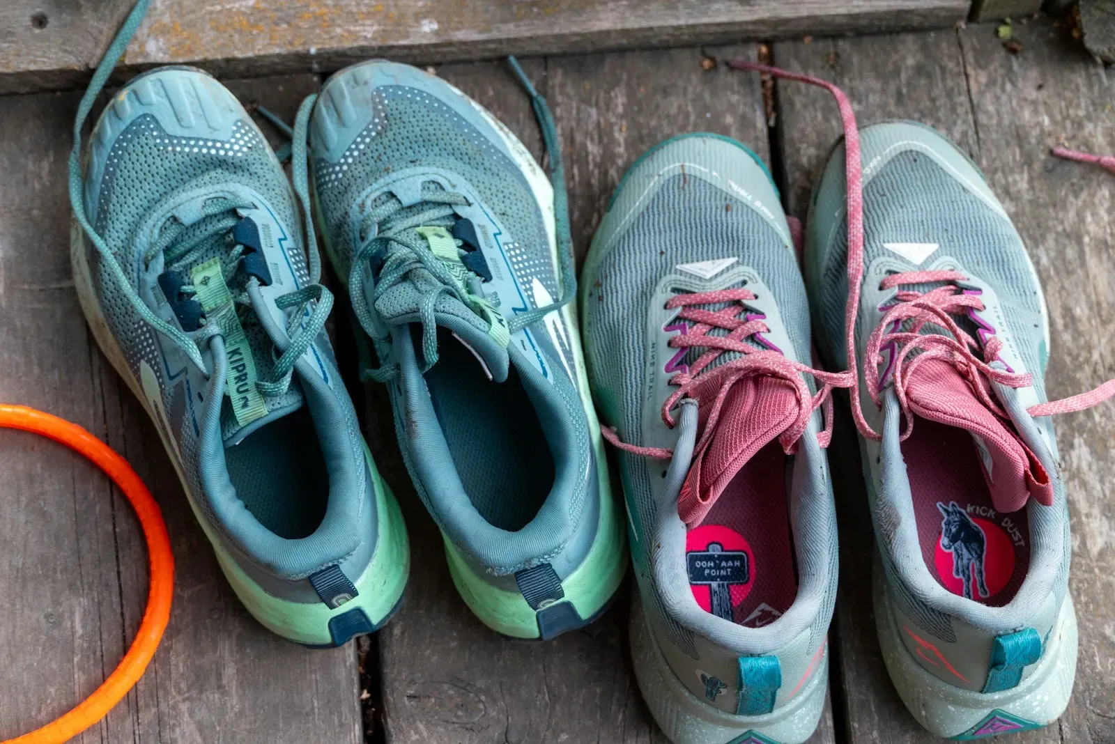 Two pairs of trail running shoes on a wooden deck