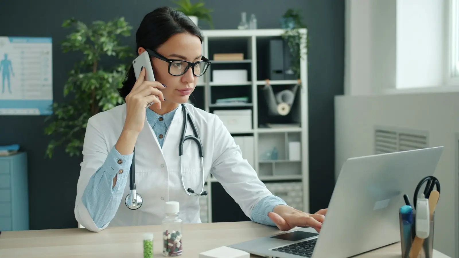 Doctor on a call while booking at her laptop
