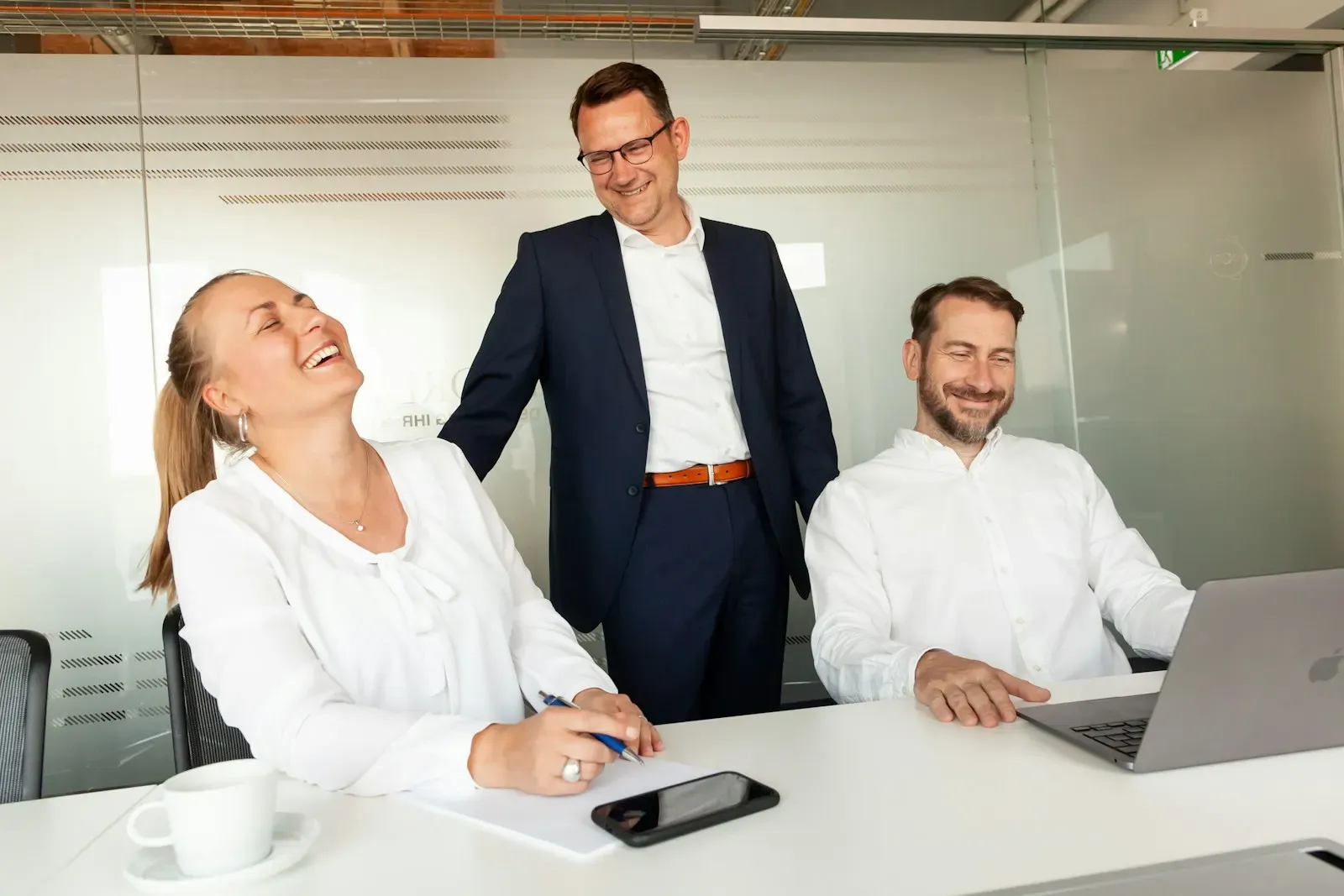 Three colleagues laughing together at a desk