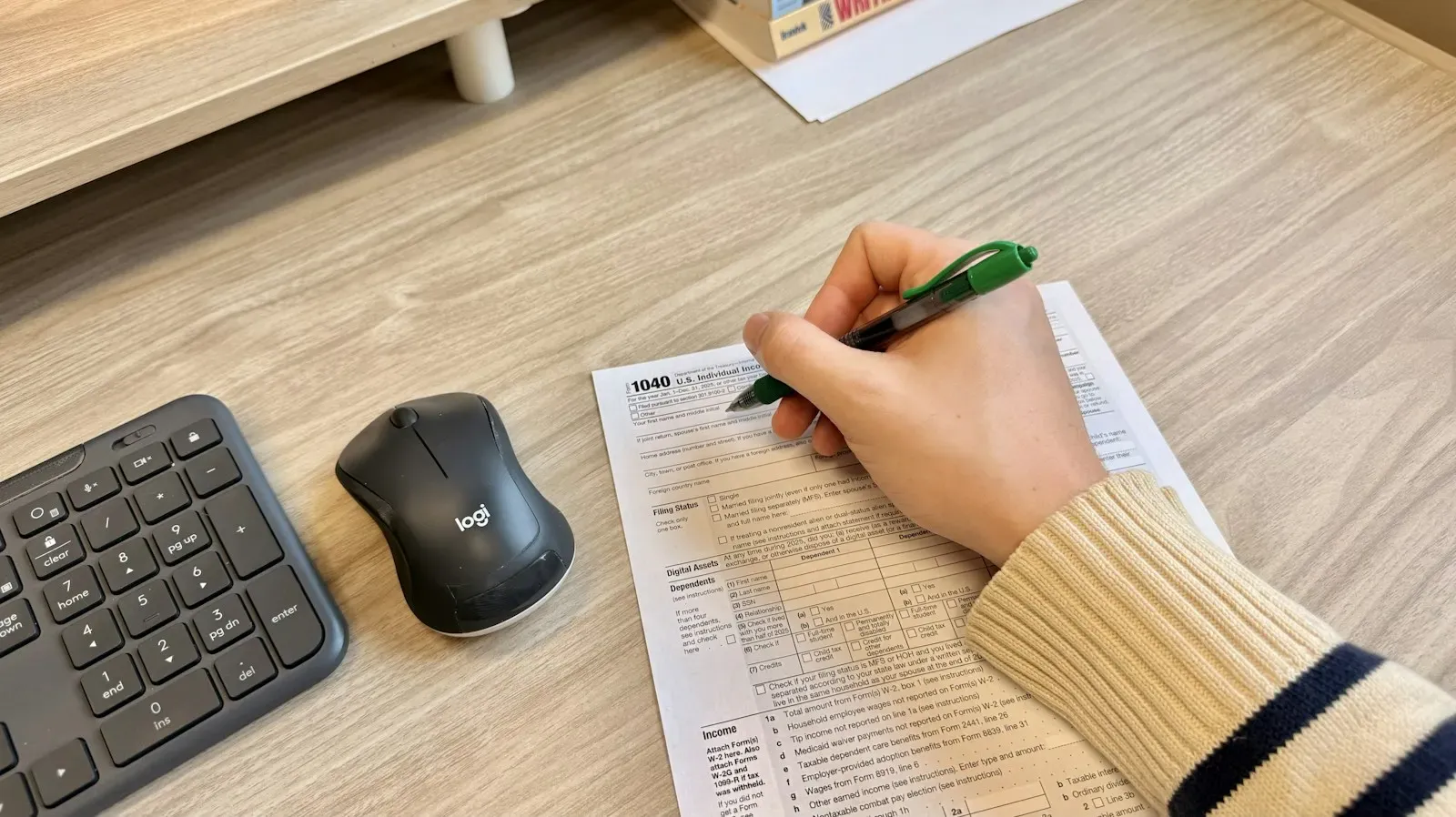 Hand writing on a printed form next to a keyboard and mouse