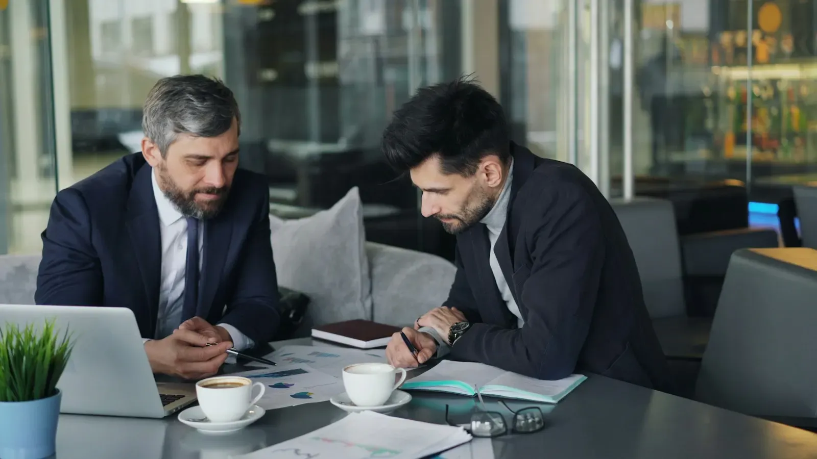 Two men in suits reviewing figures at a laptop