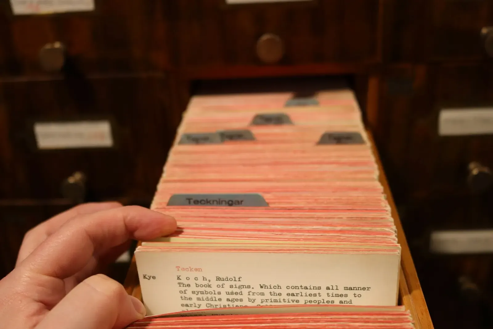 Hand pulling an index card from a wooden library card catalog
